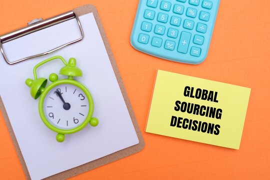 A calculator, alarm clock on a clipboard, and a sticky note with "GLOBAL SOURCING DECISIONS" text on an orange background. Symbolizing strategic business planning and time management