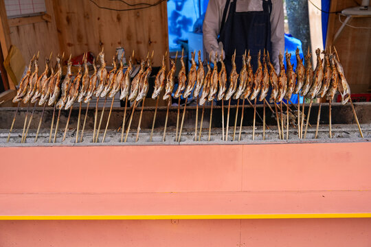 Traditional Japanese grilled called &ldquo;Ayu&rdquo; fish on wooden skewers salt-roasted over charcoal at an outdoor street food market stall.