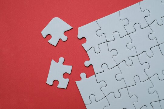 White jigsaw puzzle with missing pieces separated on a red background. Concept of problem solving, teamwork, business strategy, and incomplete solutions