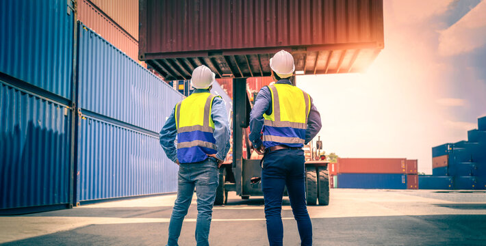 Two Engineer or foreman wears PPE checking container storage with cargo container background at sunset. Logistics global import or export shipping industrial concept.