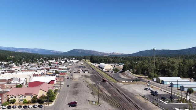 Aerial of small town Cle Elum Washington with railroad tracks with surrounding mountains featuring commercial buildings residential homes and mountain backdrop in summer