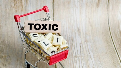 Miniature shopping cart filled with letter tiles and a wooden block spelling the word "TOXIC". © FaizAhmad