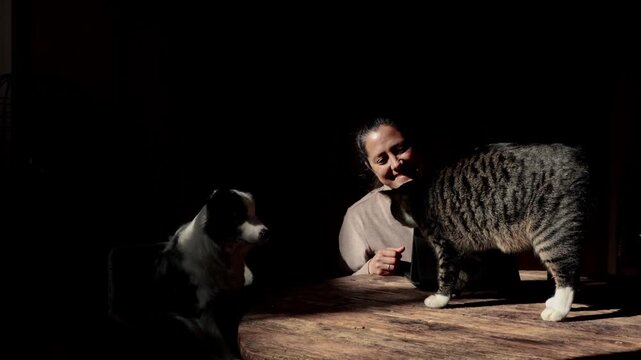 Affectionate woman petting her cat and dog at a wooden table
