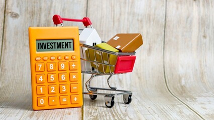 Shopping cart containing houses next to a calculator with the text INVESTMENT displayed. © FaizAhmad