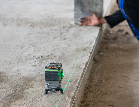 Green laser level tool projecting a precise alignment line on a concrete structure at a building construction site.
