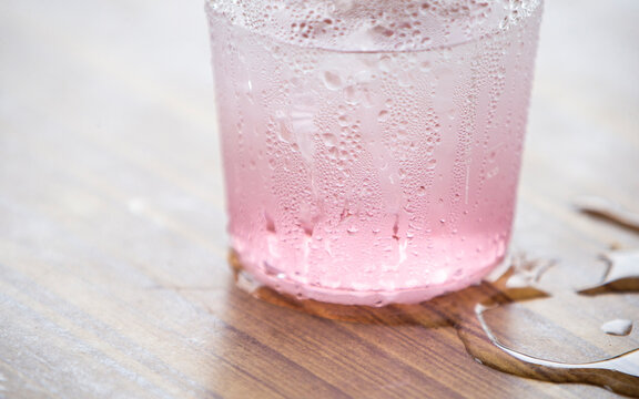 Macro shot of condensation water drops on a glass with pink beverage on wooden table.