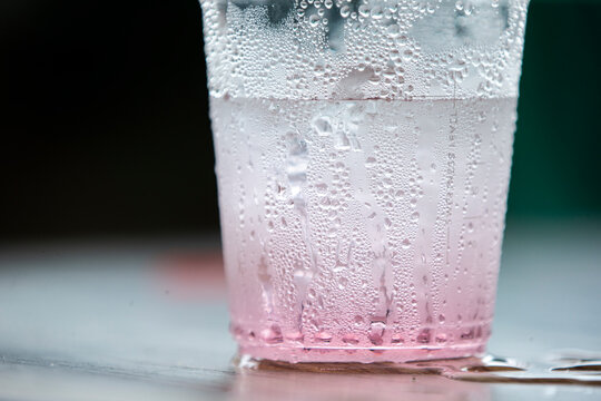 Macro shot of condensation water drops on a plastic cup with pink beverage.   A stunning macro close-up capturing a cold, refreshing pink drink inside a clear plastic cup.
