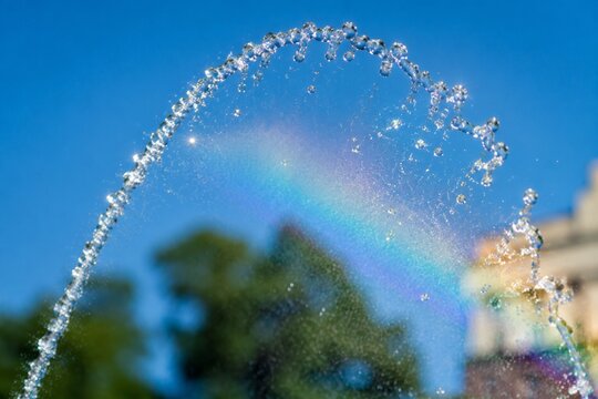 A fountain's water jet arching against a blue sky with sunlight creating glints.