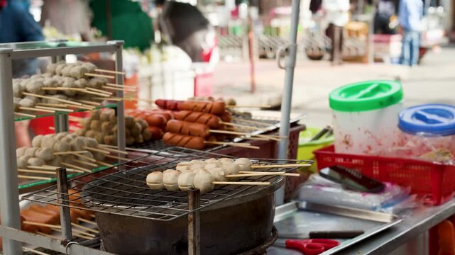 Thai Street Food Vendor Grilling Meatball and Sausage Skewers