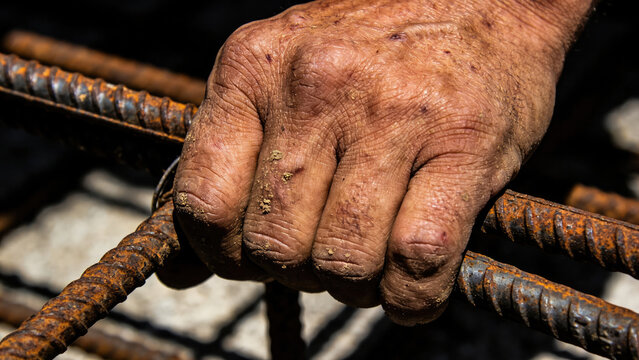 Close-up of a calloused hand gripping rusty rebar on a construction site.