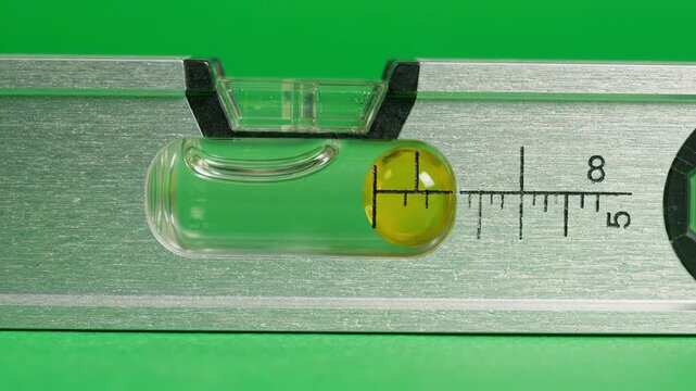 Macro shot of a professional spirit level tilting on a green screen background showing the yellow bubble moving inside the liquid vial