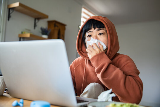 Young adult with cold working from home on laptop