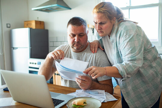 Stressed couple reviewing household bills at kitchen table