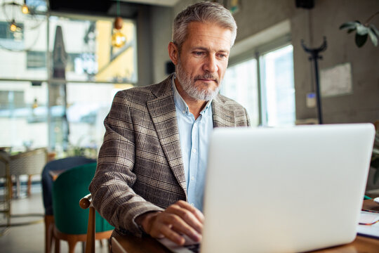 Senior man working on laptop in modern cafe
