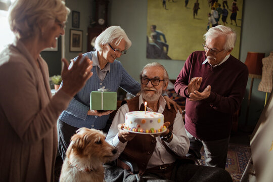 Elderly friends celebrating birthday at home with cake