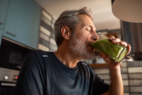Older man drinking green smoothie in home kitchen