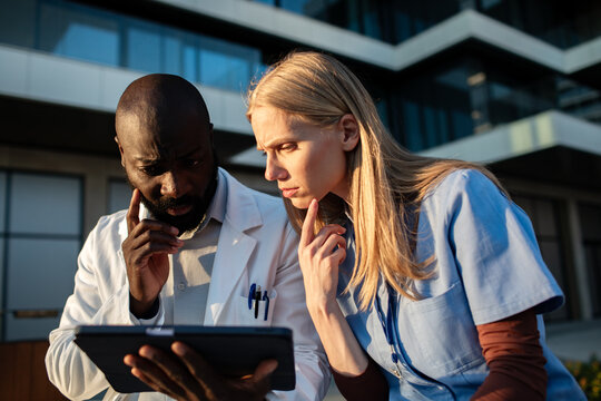 Two healthcare professionals reviewing tablet outside hospital