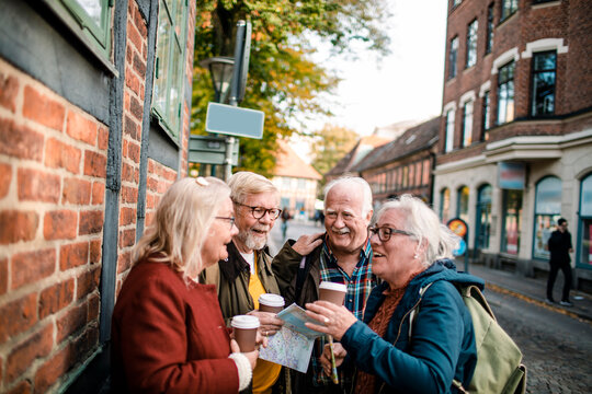 Senior friends exploring historic city street with coffee and map