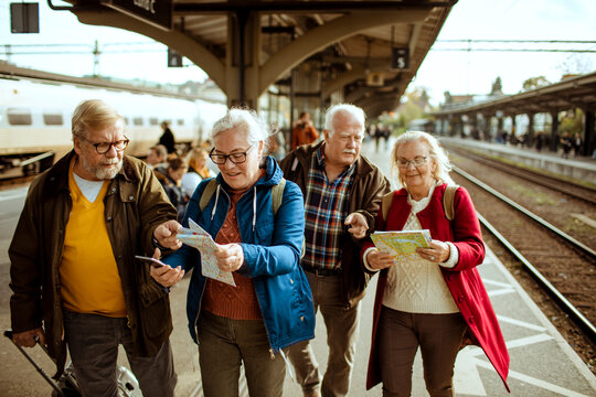 Senior travelers reading maps together at train station platform