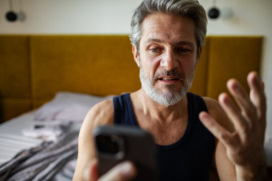 Middle-aged man frustrated with smartphone in bedroom at home