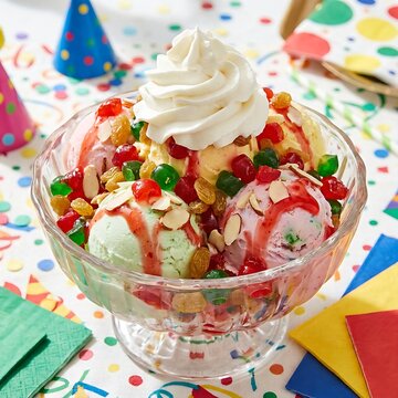 A colorful traditional tutti frutti sundae featuring mixed fruit flavored ice cream scoops, loaded with chopped candied fruits, raisins, almonds, and a drizzle of sweet strawberry syrup. Finished with
