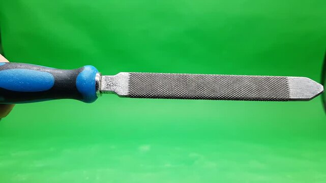 Metal hand file tool rotating slowly against a bright green screen background for video editing and compositing work