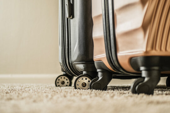 Low angle close up shot of dual spinner wheels of two modern hard shell suitcases standing on a textured beige carpet. Concept of packing, trip preparation, departure, and travel details.