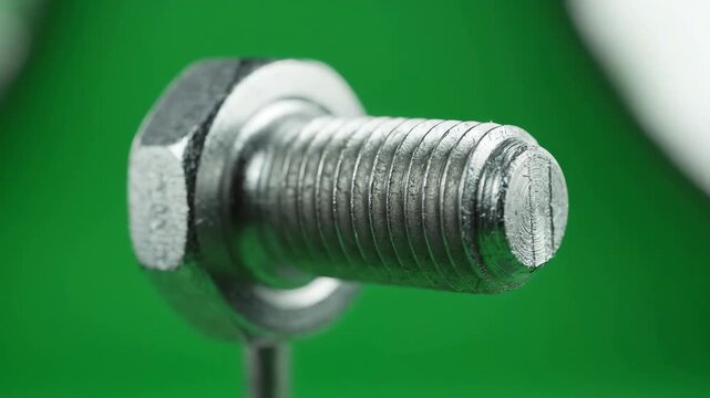 Polished stainless steel industrial bolt rotating slowly against a solid green screen background for chroma key compositing