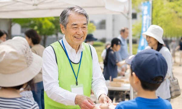 地域イベントで子どもと交流する笑顔のシニアボランティアスタッフ