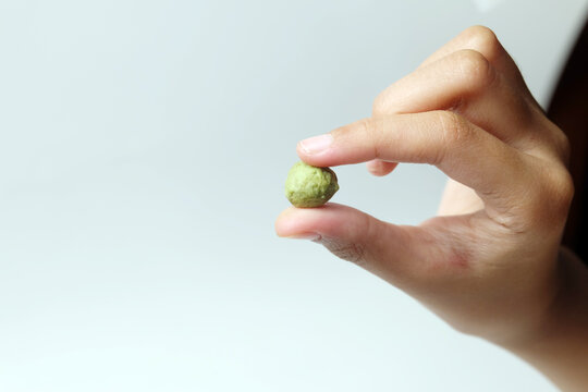 hand pinching a single small green crispy snack ball between two fingers against a white background.