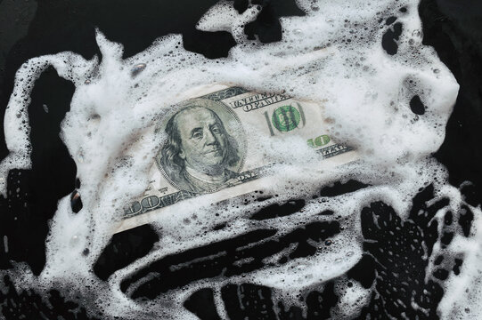 100 dollar bill lies in white foam on a baking sheet. View from above. Concept of money laundering, criminal and shadow business.