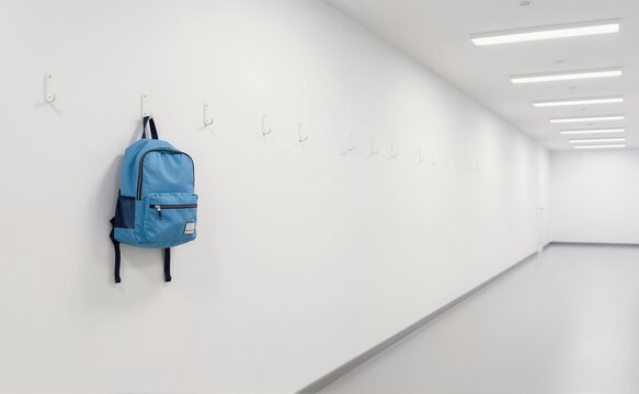 Blue backpack hanging on a white wall hook in an empty modern hallway
