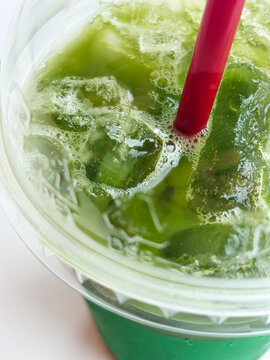 Macro Top View of Refreshing Iced Green Tea Matcha with Red Straw. Extreme macro top-angle shot of refreshing iced green tea matcha with crystal clear ice cubes,