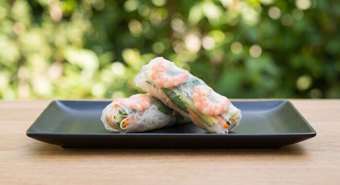 Freshly made Vietnamese spring rolls filled with shrimp, vegetables, and herbs served on a black plate.