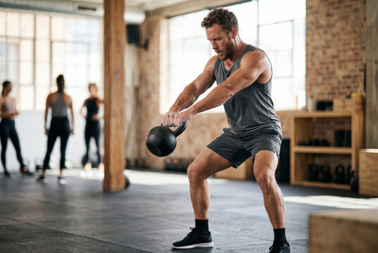 Athletic man performing kettlebell swing exercise in gym