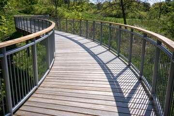 Obraz premium Curved wooden walkway with metal railings in a sunny park setting