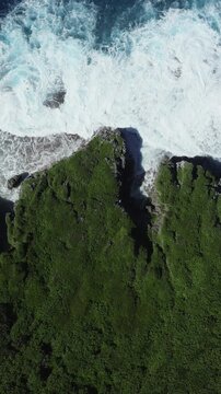 Aerial view of powerful ocean waves crashing against the rugged green coastline of Niue in the South Pacific.
