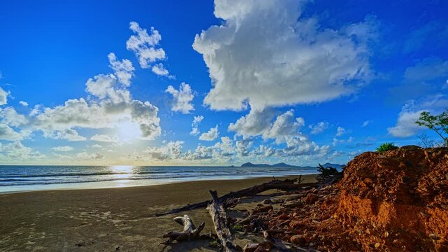 Time lapse sunset sky over the Ancient coastal forest remains lying across the shoreline where powerful ocean waves have eroded the beach, exposing roots and leaving behind massive wooden stumps.