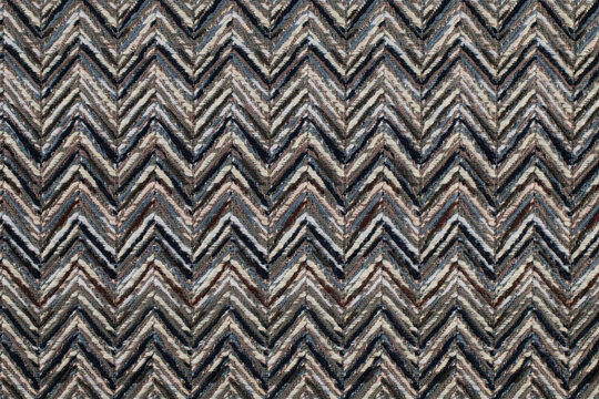 Close up of a woven fabric with a repeating chevron zigzag pattern in shades of dark blue, grey, brown, and cream with a textured finish