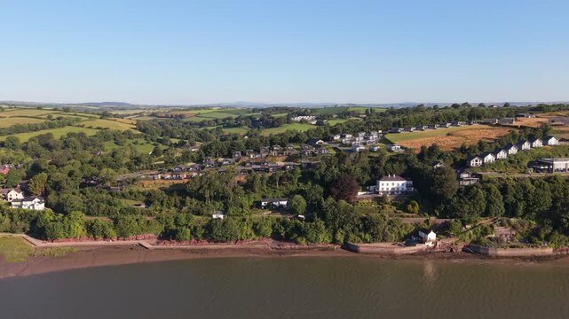 Aerial drone footage of the historic village of Laugharne in Carmarthenshire, Wales, featuring the River Coran estuary, traditional buildings, surrounding countryside and picturesque rural landscape 