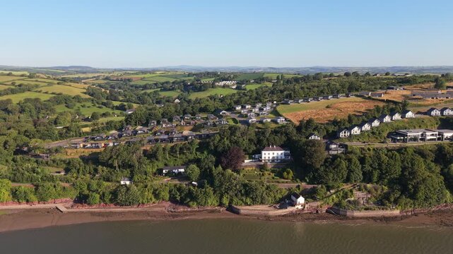 Aerial drone footage of the historic village of Laugharne in Carmarthenshire, Wales, featuring the River Coran estuary, traditional buildings, surrounding countryside and picturesque rural landscape 