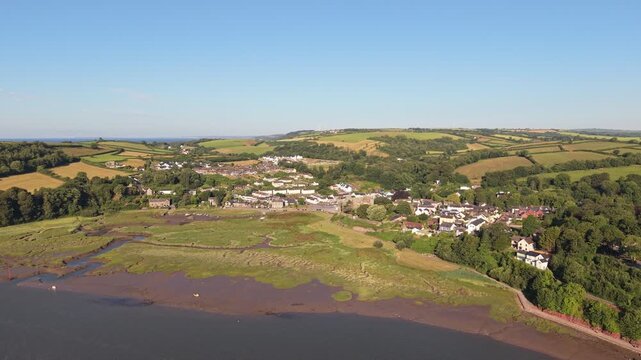 Aerial drone footage of the historic village of Laugharne in Carmarthenshire, Wales, featuring the River Coran estuary, traditional buildings, surrounding countryside and picturesque rural landscape 