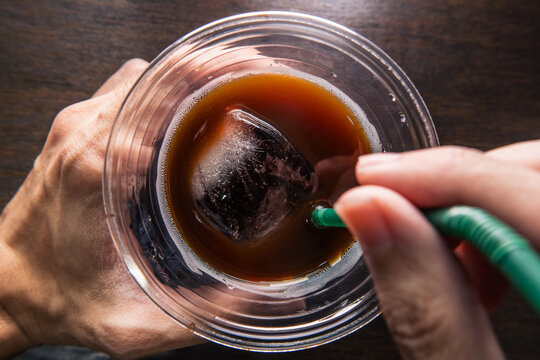 POV view of Drinking Iced americano coffee in single use plastic cup with straw