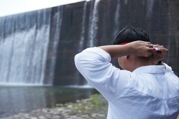 Rear view of a man adjusting a red and white headband beside Tukad Unda Waterfall in Klungkung, Bali, preparing for an Indonesian Independence Day themed moment. © mrbudiarto