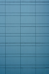 Fototapeta premium Teal blue architectural cladding panels forming a minimalist geometric grid on a modern building facade.