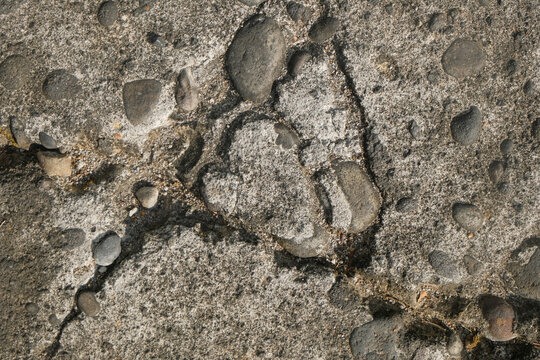 Close-up of a weathered concrete surface with embedded pebbles and exposed aggregate stones. Durable construction material texture for architectural backgrounds. Engineering, infrastructure