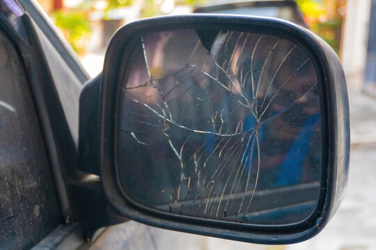 Close up view of a broken and badly cracked side mirror glass on a car. Damaged vehicle part template for car insurance claims, traffic accident, or automotive repair concept.