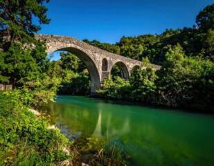 Fototapeta premium Ancient stone arch bridge spanning a calm green river.