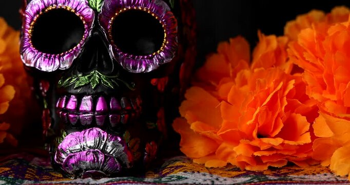 Horizontal slide shot revealing a traditional Day of the Dead altar with metallic black skull, orange marigold flowers and glowing candles.