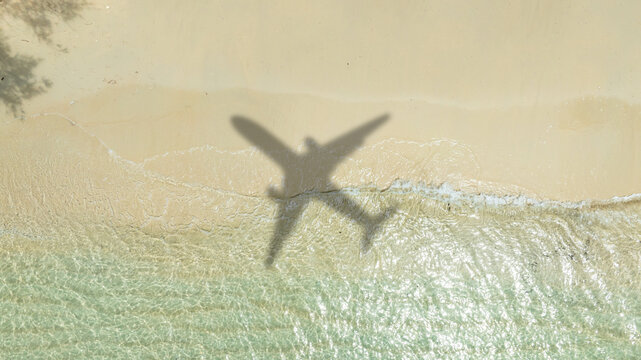 Aerial view of shadow passenger plane silhouette and sandy beach blue sea with waves at sea beach summer vacation sea travel concept	
